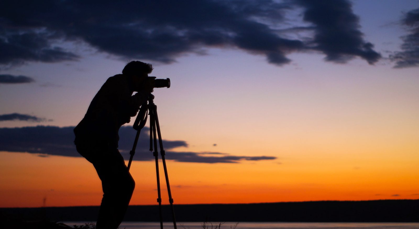 Silhouette of a person taking a photograph at sunset